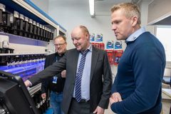 Miehet käyttävät automaalilaitteistoa. Yksi osoittaa näytöltä asioita kahdelle muulle henkilölle.