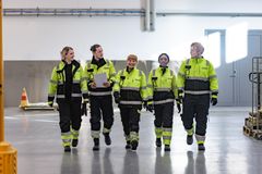 Henkilöt kävelevät rivissä hallissa keltaiset huomioasut päällään.