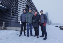 Henkilöt seisovat talvisessa peltomaisemassa. Takana navetta.