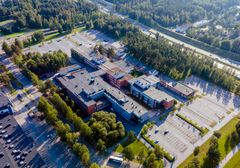 Ilmakuva suuresta rakennuskompleksista puiden ympäröimänä, pysäköintialueet näkyvät etualalla.