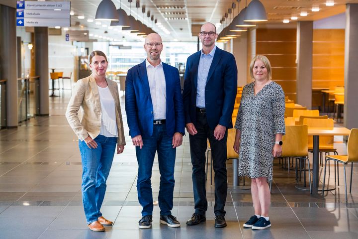 Neljä henkilöä seisoo rivissä sisätiloissa.