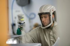 Henkilö suojavarusteissa maalaa autoa.