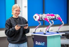 Nainen ohjaa robottikoiraa kaukosäätimellä sisätiloissa.