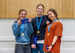 Kolme hymyilevää nuorta seisoo yhdessä mitaleineen.