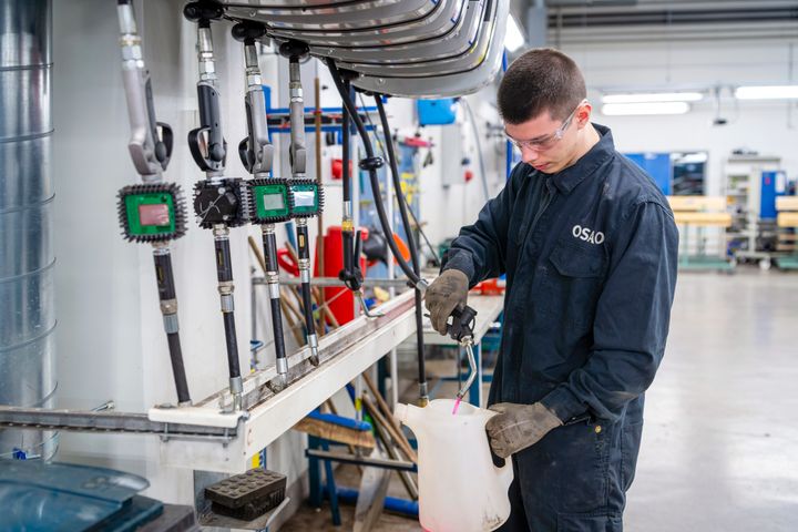 Mies työskentelee teollisuusympäristössä suojavaatteissa.