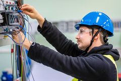 Mies työskentelee sähkökaapin parissa käyttäen suojakypärää ja -laseja.