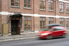 Punainen auto ajaa ohi tiilirakennuksen, jossa on suuria ikkunoita.