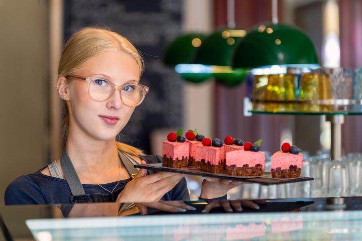 Henkilö pitelee tarjotinta, jolla on useita leivoksia.