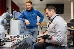 Kaksi miestä työskentelee elektroniikkalaitteiden kanssa sisätiloissa.