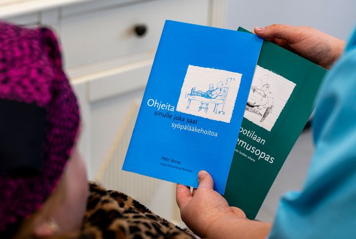 Henkilö pitelee kahta opasta saattohoidosta ja syöpähoidosta.