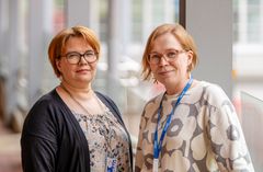 Valokuva kahdesta henkilöstä sisällä, he katsovat kameraan.