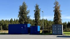 Kolme suurta konttia pysäköitynä ulkoalueelle, taustalla puita ja selkeä taivas.