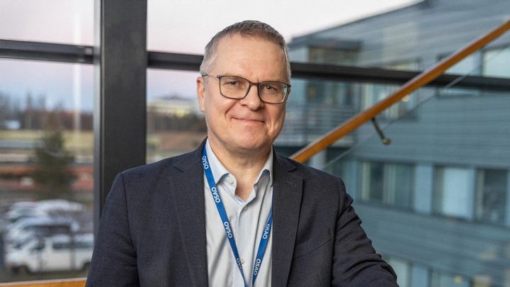 Silmälasipäinen mies tummassa puvuntakissa seisoo toimistorakennuksessa.