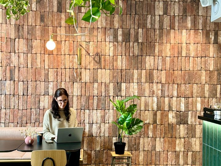Nainen työskentelee kannettavalla tietokoneella viihtyisässä kahvilassa viherkasvien ympäröimänä.