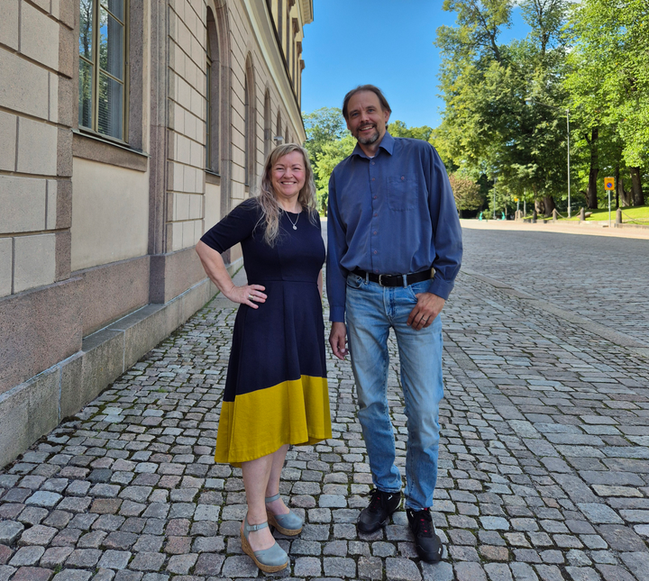 Nina Ekman ja Tero Nyman seisovat ulkona kivetetyllä kadulla ja hymyilevät kameralle.