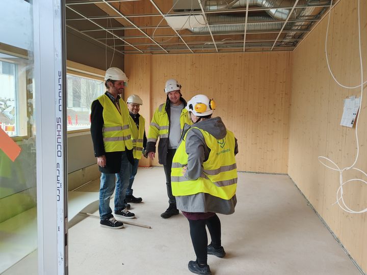 Nelj%E4%20henkil%F6%E4%20keskustelemassa%20rakennuksen%20sis%E4ll%E4%2C%20kaikilla%20on%20kyp%E4r%E4t%20ja%20huomioliivit%20p%E4%E4ll%E4.