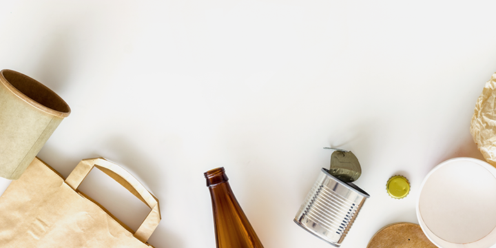 Paperi- ja lasiastia, säilykepurkki, pullonkorkki ja kankainen ostoskassi valkealla taustalla.