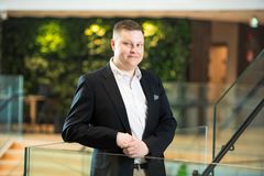 Tuomas Salminen kuvattuna Ilmalan aulassa: taustalla vaaleaa puuta ja vihreää. Salminen hymyilee kuvassa.