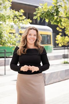A woman standing outdoors, with a tram in the background.