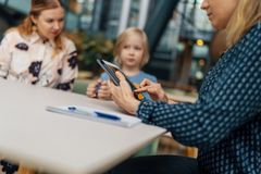 Kolme henkilöä istuu pöydän ääressä, yksi heistä käyttää tablettia.