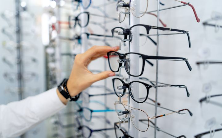 Henkilö valitsee silmälasit telineestä optikkoliikkeessä.