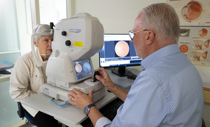 Optometristi suorittaa silmien tutkimuksen naiselle silmien- ja näöntutkimuksen laitteella.