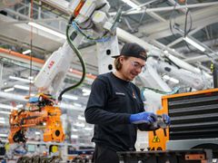 Mechanic inserting components into an AGCO Power engine in the engine assembly plant in Nokia Finland with a robot in the background.