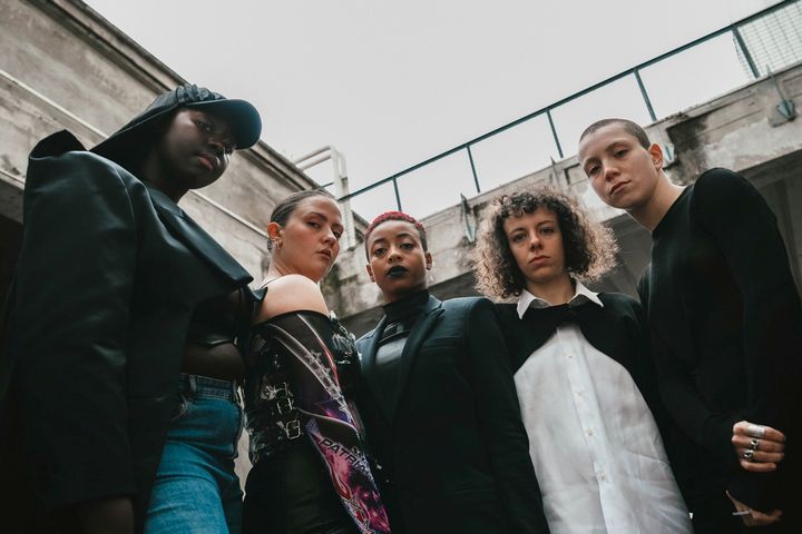 Viisi esiintyjää katsoo kameraan.