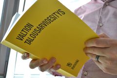 Henkilö pitelee käsissään keltaista kirjaa, jonka kannessa lukee "Valtion talousarvioesitys".