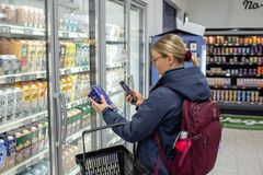 Nainen tutkii ruokapakkausta puhelimella ruokakaupassa.