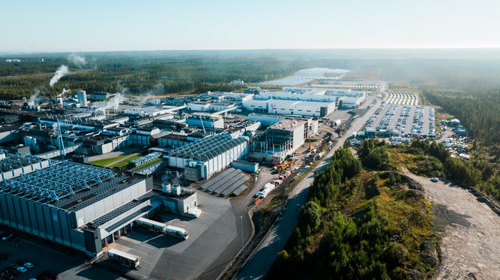 Ilmakuva laajasta teollisuusalueesta metsän ja vesistön vieressä.