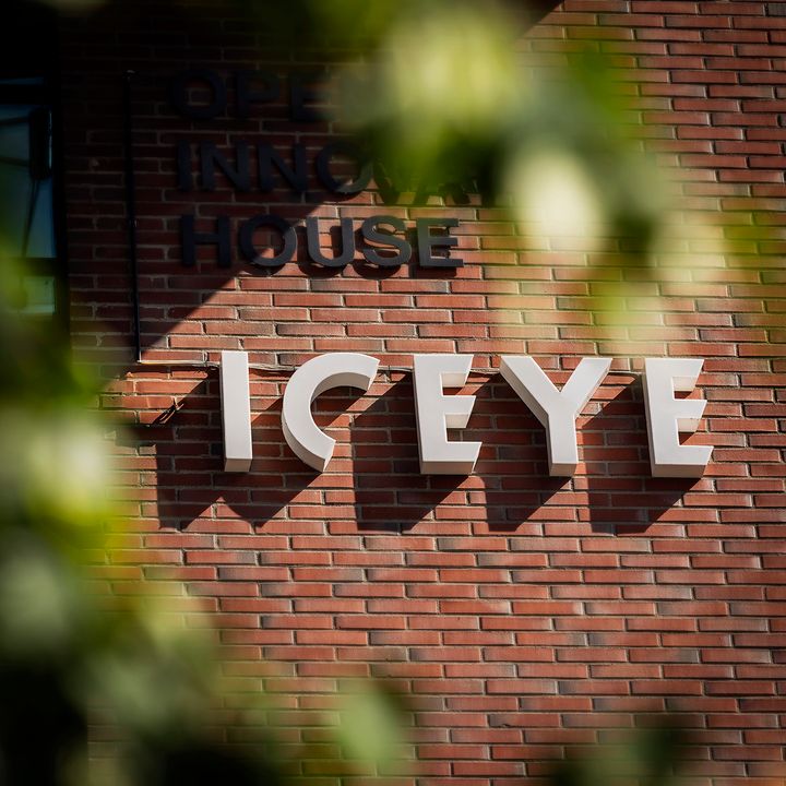 "Close-up of a brick building with the word 'ICEYE' prominently displayed on the facade, partially framed by blurred foliage."