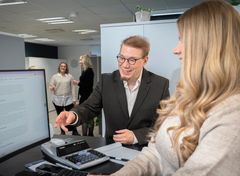 Kaksi henkilöä, mies ja nainen, työpaikallaan Wulff Tilitoimistojen Raahen toimipisteessä. Keskustelu pöydän äärellä.