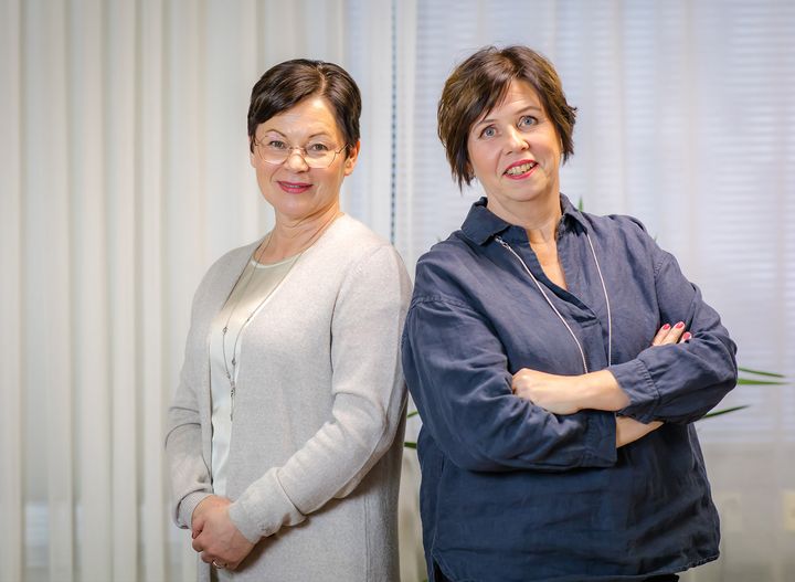 Kaksi naista, tilitoimistoammattilaisia, seisoo vierekkäin hymyillen kameralle.