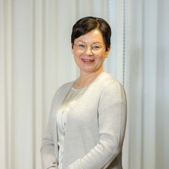 Hymyilveä nainen vaaleassa asussa, tummat hiukset.