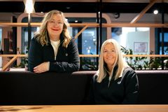 Kaksi naista toimistoympäristössä, mustat paidat. Iloiset, innokkaat ilmeet ja rento asento.