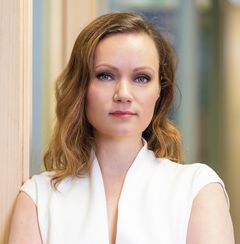 Kasvokuva naisesta valkoisessa paidassa, pitkät ruskeat hiukset, keskittynyt ilme.