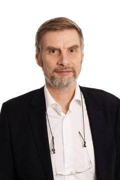 En person i mörk kostym står och tittar mot kameran.