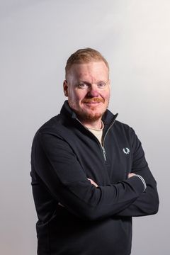 Vaaleahiuksinen mies, katsoo kohti kameraa. Iloinen ilme, musta paita.