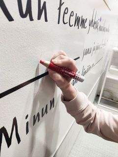 Lähikuvassa STABILO MARKdry -valkotaulukynä ja käsi. Punainen kynä, jolla kirjoitetaan isolla valkotaululle.