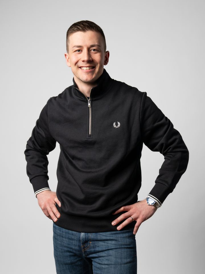 Noin 30-vuotias mies, tummat hiukset, hymy, musta paita.