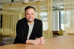 Mis tummassa neuleessa ja vaaleassa paidassa, nojaa pöytään, vaalea toimistoympäristö, sisätilat