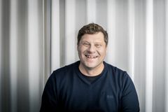 kuvassa mies mustassa neulepaidassa, katsoo ja hymyilee kameralle