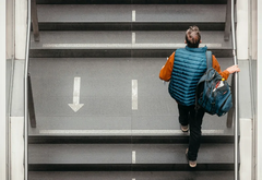 Henkilö nousee julkisen tilan portaita, reppu olalla.