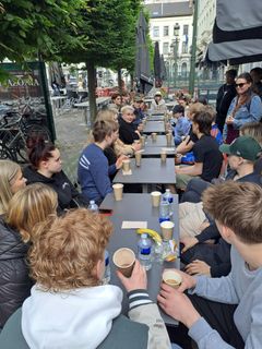 Nuoret istuvat pitkän ulkopöydän ääressä keskustelemassa. Taustalla rakennuksia Brysselissä.