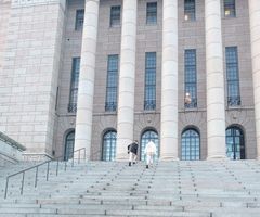 Kaksi ihmistä kävelee eduskuntatalon portaita ylös.