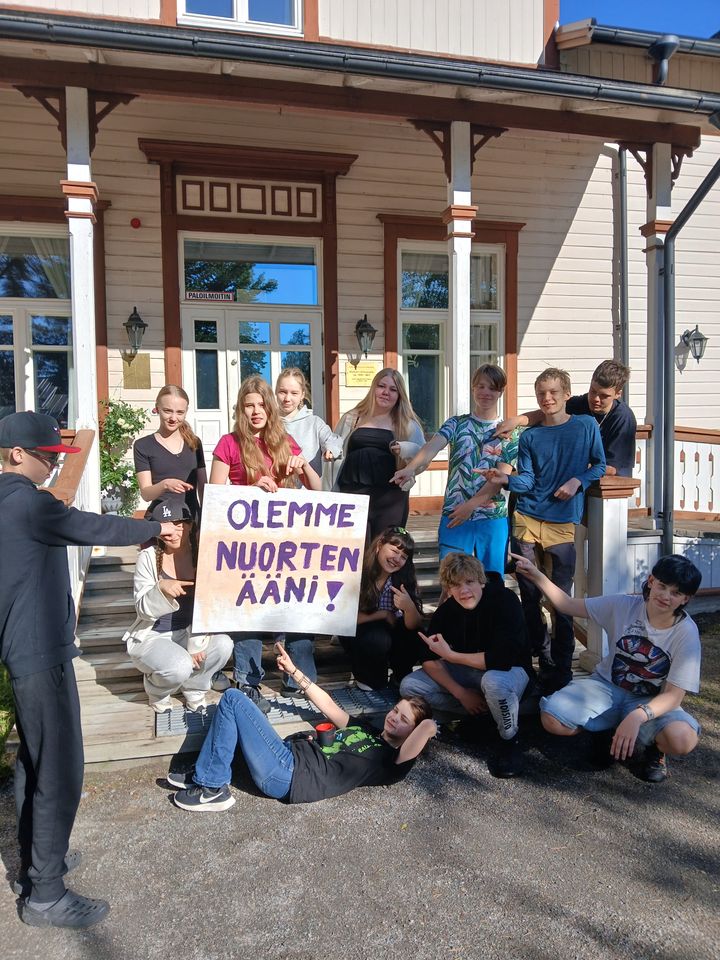 Nuoria%20seisomassa%20ja%20istumassa%20yhdess%E4%20Nuorisokeskus%20Marttisen%20edustalla%20pit%E4en%20kyltti%E4%2C%20jossa%20lukee%20%22Olemme%20nuorten%20%E4%E4ni%22.
