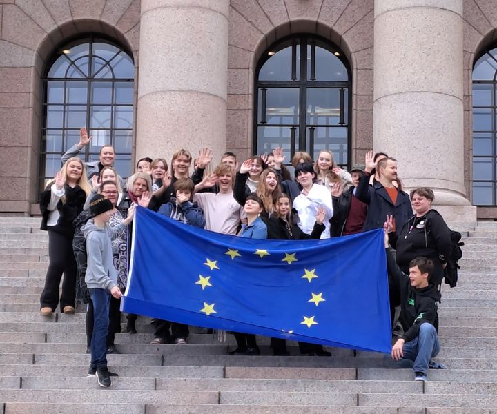 Ryhmä nuoria Euroopan unionin lipun kanssa eduskunnan portailla.
