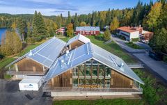 Ilmakuva Hyytiälän metsäasemasta, etualalla moderni, puinen päärakennus, taustalla järvi ja metsää sekä aseman vanhemmat rakennukset.