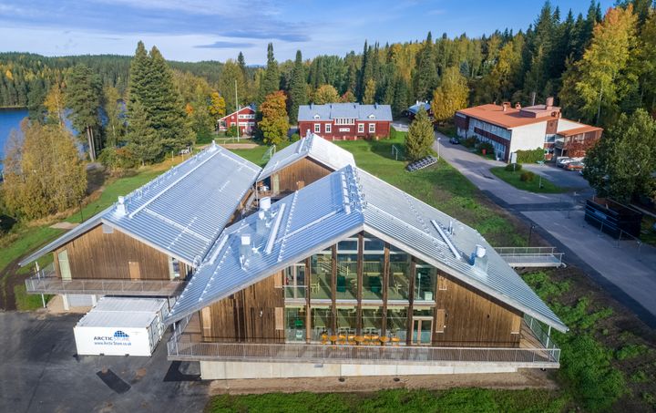 Ilmakuva Hyytiälän metsäasemasta, etualalla moderni, puinen päärakennus, taustalla järvi ja metsää sekä aseman vanhemmat rakennukset.